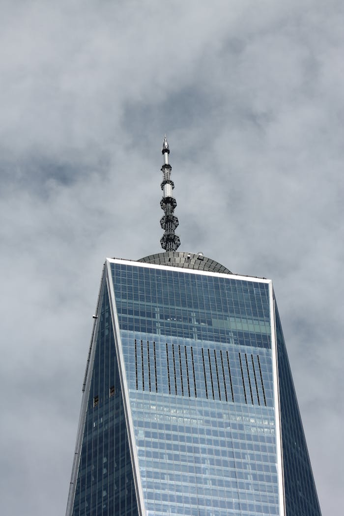 Close-up view of One World Trade Center's spire on a cloudy day in New York City.